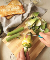 Anonymous person peels artichoke in kitchen at home. Healthy eating and traditional Italian dish. Fresh seasonal farm produce.