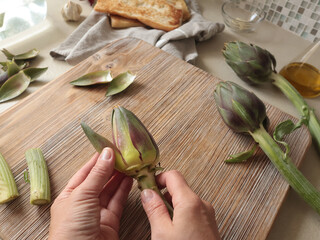 Anonymous person peels artichoke in kitchen at home. Healthy eating and traditional Italian dish. Fresh seasonal farm produce.