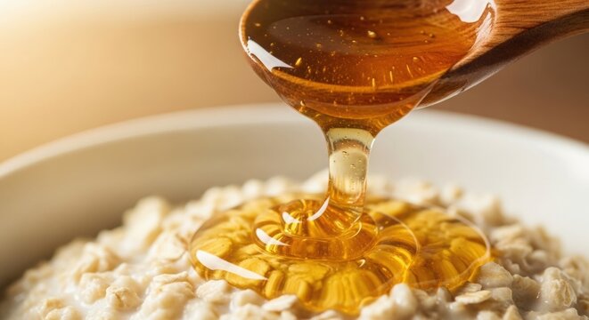 Golden honey dripping from wooden spoon onto creamy oatmeal breakfast bowl - Powered by Adobe