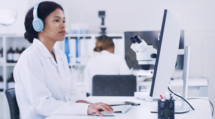 Computer, headphones and science with woman in laboratory for medical research or pharmaceuticals. Healthcare, music and typing with scientist at desk for work on clinical trial or experiment