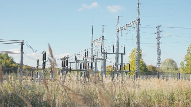 High-voltage electrical substation in a rural field surrounded by dry grass under a clear blue sky, showcasing energy infrastructure and power distribution network.
