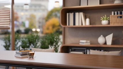 Coffee cup and eyeglasses on book on wooden table across display shelf and glass wall in living room