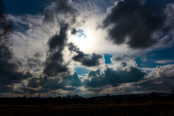 Sun's powerful rays pierce through a dramatic tapestry of dark, heavy storm clouds. A moody sky scene over a silhouetted land