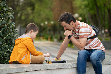 Boy with father playing chess outdoor.