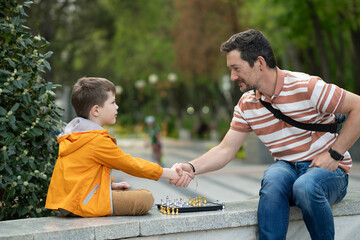 Boy with father playing chess outdoor. Handshake, clasp, handclasp.