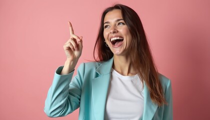 Laughing girl points finger up, gets bright idea. Woman in aqua jacket poses in studio. Brainstorm presentation with joyful student at pink backdrop. Positive model looks happy, excited and cheerful.
