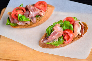 
Bruschetta with ham, salad and cherry tomatoes on a white plate