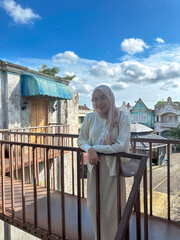Woman stands happily on a balcony, surrounded by colorful buildings under a bright blue sky