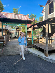 A young woman strolls down a rustic path in an old village under a clear blue sky