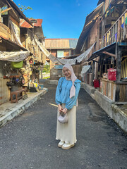 A young woman stands happily on a sunny street in a village with wooden houses and vibrant details