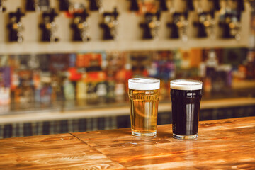 Two Distinct Glasses of Beer on Wooden Bar Counter in Lively Pub Atmosphere Against Taps
