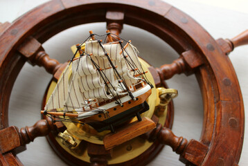 Blurred wooden yacht wheel with copper parts and sailing ship figurine in it center  