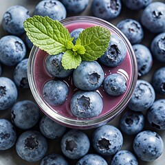 Glass of vibrant blueberry smoothie with fresh mint leaves and whole berries Ripe blueberries are scattered around on a