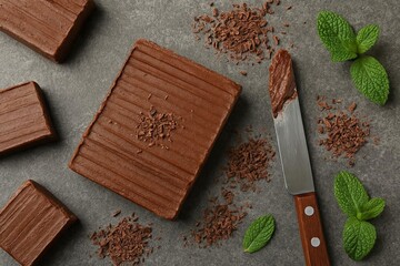 Three textured chocolate blocks scattered chocolate shavings a knife with chocolate spread and fresh mint leaves on a