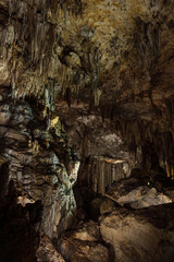 Wide Limestone Cave Chamber with Stalactites, Rock Layers, and Moody Warm Light