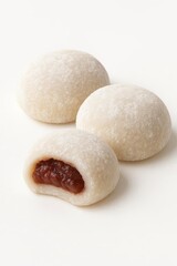 Three traditional Japanese mochi rice cakes with sweet red bean paste filling One is sliced showing the anko on white