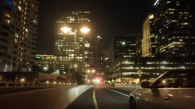 Cinematic view of a white convertible sports car driving along Miami city streets at night, with illuminated skyscrapers and city lights in the background	
