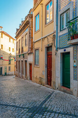 Narrow empty cobblestone street with colorful tiled facades and traditional doors in of Lisbon city, Portugal. Medieval alley in old town of Lisboa. Vertical orientation. Travel and tourism in Europe