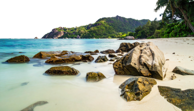 Tropical beach, blue ocean, rocks, & green mountains in background