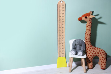 Height measuring chart on pale green wall and toys indoors, space for text