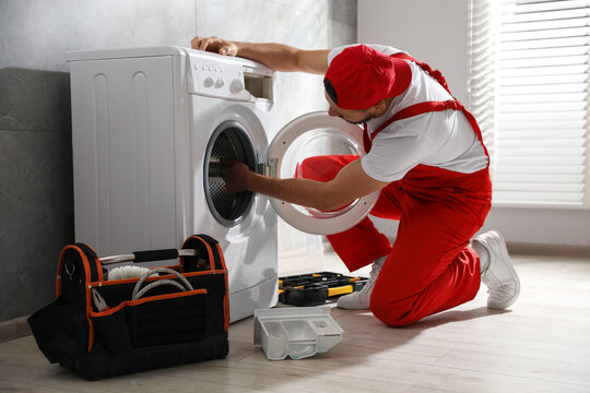 Professional repairman fixing broken washing machine indoors