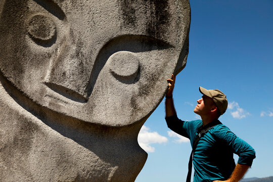Western male tourist, poses with the Palindo megalith, located in the Bada Valley, Central Sulawesi, Indonesia