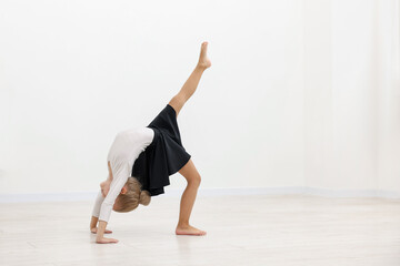 Naklejka premium Little girl doing gymnastic exercise on floor near white wall indoors. Space for text