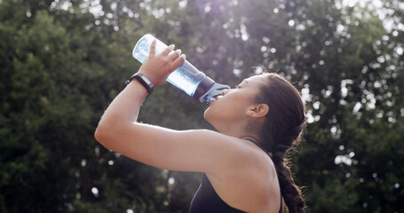 Woman, drinking water and fitness in park, break and profile with hydration, tired and electrolytes in nature. Girl, bottle and aqua for detox, thirst or fatigue with training routine in Colombia