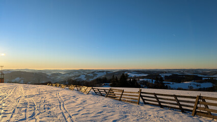Winter ski slope with sunset over snowy mountains