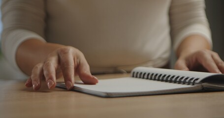 Close up of a woman hand resting on an open spiral notebook placed on a wooden table, capturing an intimate and creative work moment.