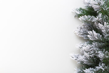 Green artificial fir branches covered with hoarfrost and white snow on light gray table background. Closeup. Empty place for text. Top down view.