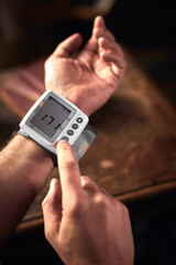 Man checking blood pressure and heart rate at home with a portable modern digital meter.