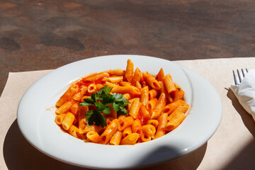 Penne arrabiata - traditional italian pasta with spicy sauce on a table