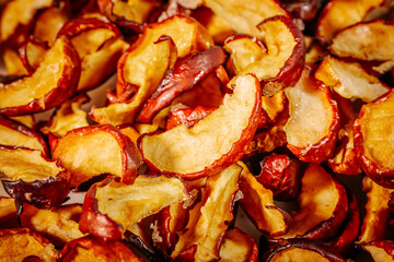 A detailed macro image showing the texture and rich color of dried apple slices, highlighting their wrinkled, red skin and golden flesh.