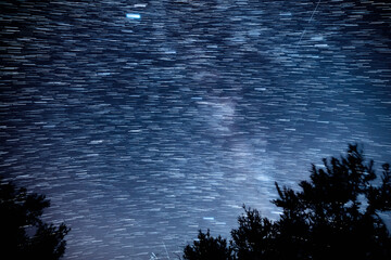 Milky way star-trails and constellations with landscape silhouettes photographed from a dark countryside location.