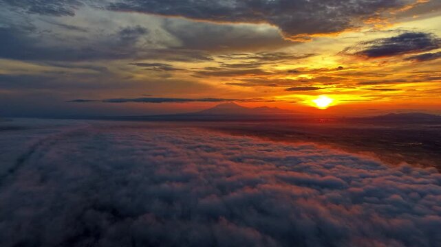 Aerial view of a fiery sunrise over a sea of fluffy clouds, illuminating the distant lawu mountains with a warm glow, Klaten Regency, Central Java, Indonesia.