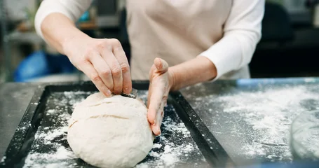 Fotobehang Bakkerij Hands, score dough or bread in bakery with blade for cooking food, restaurant cuisine or hospitality. Person, knife or ingredients in kitchen for catering, meal prep and gluten free sourdough recipe.  © peopleimages.com