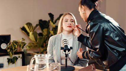 Makeup brush, beautician and presenter in recording studio for podcast, getting ready or online show. Live stream, radio broadcasting or woman with cosmetics for host, content creation and microphone
