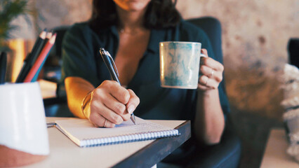 Hands, coffee and writing in notebook in home office for meeting schedule, remote work and reminder. Freelancer, personal assistant and tea with notepad for to do list, diary management and planning
