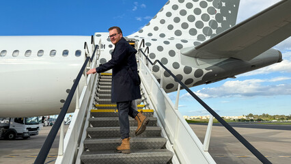Ascending stairs to polka-dotted plane, Caucasian man in adventure boots, embodies Wanderlust Day spirit and global nomad vibe