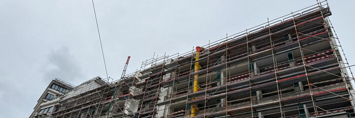 Cloud-kissed scaffolding envelops a metropolis building, echoing urban renewal vibes, May Day reconstruction, and future dwellings