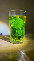 Radiant chartreuse elixir in crystal glass, verdant leaves afloat, celebrating Herbology Day, evoking spring equinox renewal rituals