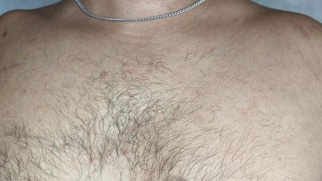 Hand of young asian or indian guy in puberty or adolescent touches hairy chest skin. Adult male person body hair growth concept. Curly haired chest extreme closeup macro side view.