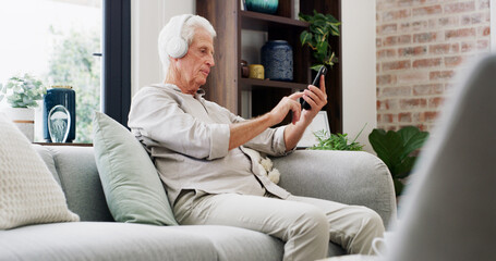 Music, phone and relax with old man on sofa in living room of home for streaming subscription. App, headphones and retirement with senior person in apartment for audio or sound entertainment