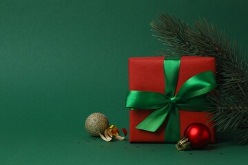 Close-up view of holiday gift box tied with green ribbon with holiday decorations on green festive...