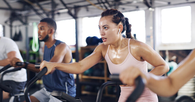 Spin class, exercise and earphones with woman in gym for intense workout, music and cycling challenge. Fitness, streaming and stationary bike machine with people in sports club with sweat and energy - Powered by Adobe