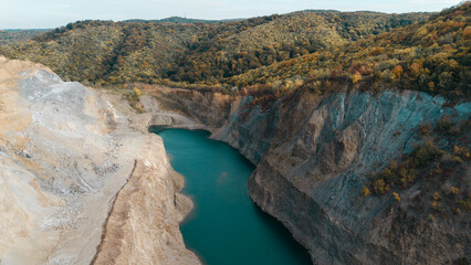 Aerial view of a flooded quarry surrounded by colorful autumn forest in Fruska Gora, Serbia. Calm turquoise water contrasts with rocky cliffs and seasonal foliage