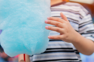 Cotton candy in the hand of a child in a summer park. Sweet food and sugar. © Kunlathida