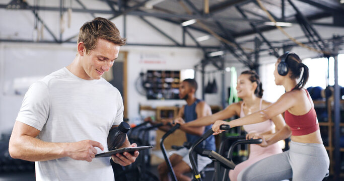 Man, personal trainer and tablet with people in spin class for fitness, schedule session and progress. Coach, digital app and tracking of cycling exercise, training performance and workout management - Powered by Adobe
