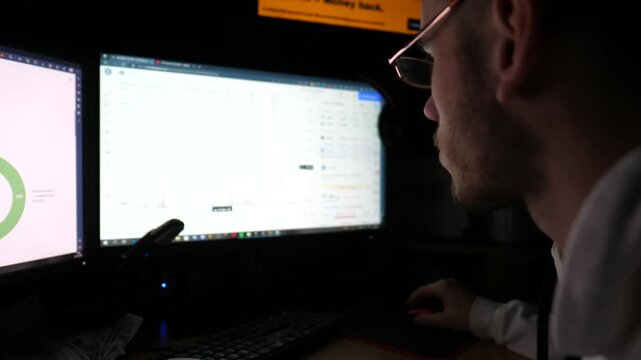 Financial analyst working on computer with multiple monitors at night. Young male broker analyzing real-time commodities and foreign exchange charts. Concept of bitcoin BTC and stock market. Slow mo